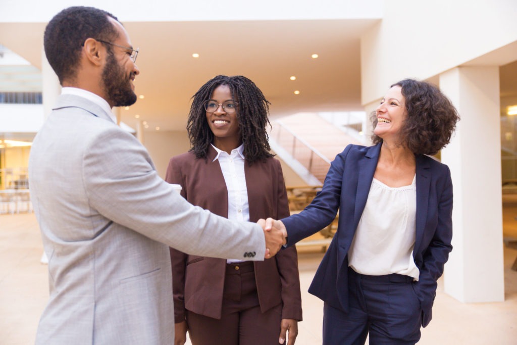 Happy business partners greeting each other. Business man and women standing in office hallway, shaking hands, smiling, talking. Business communication concept