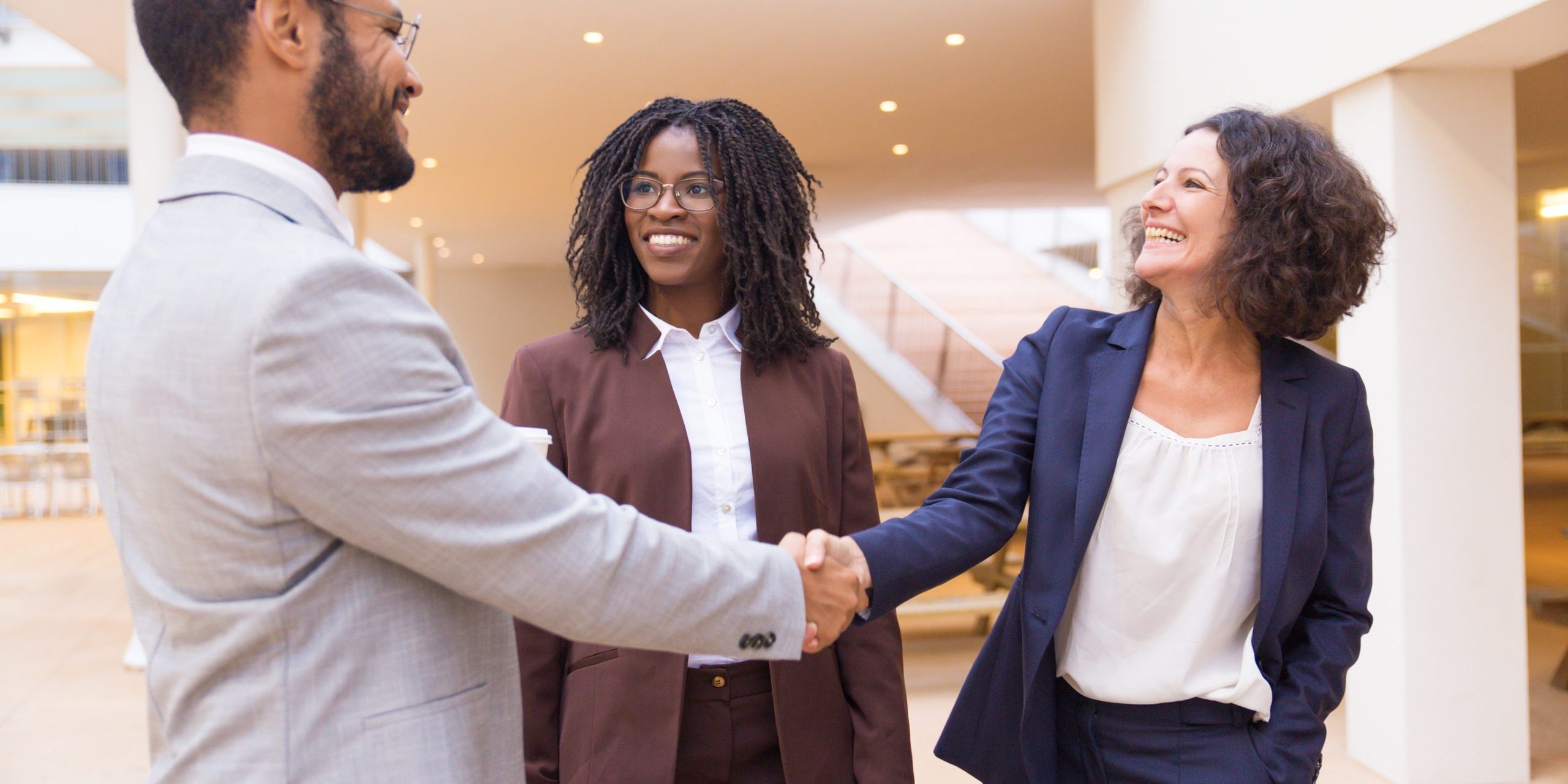 Happy business partners greeting each other. Business man and women standing in office hallway, shaking hands, smiling, talking. Business communication concept